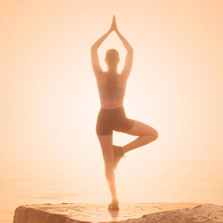 Frau auf einem Bein im Gegenlicht in einer Yogapose